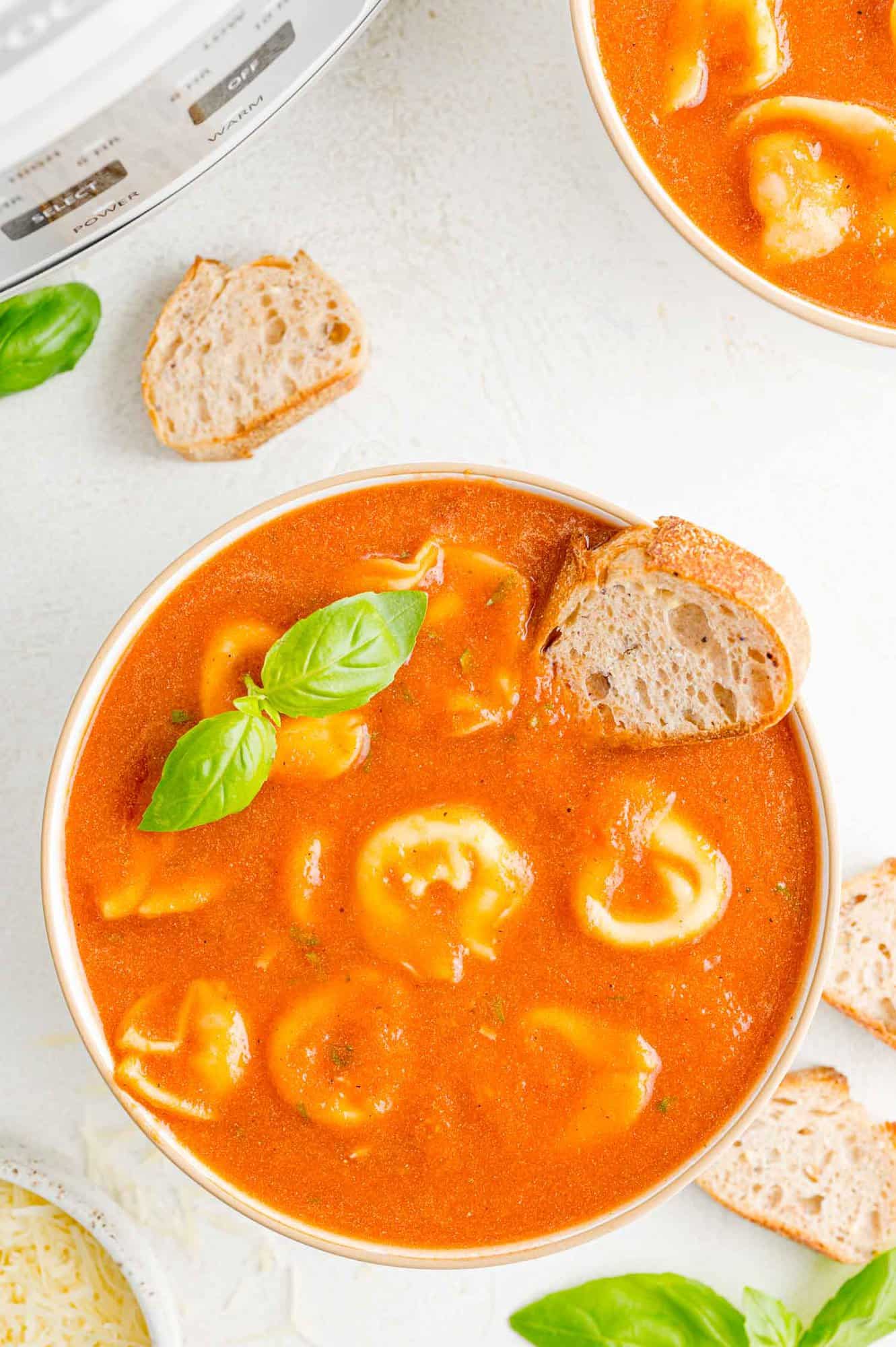 White bowl containing tomato soup with tortellini, garnished with fresh basil.