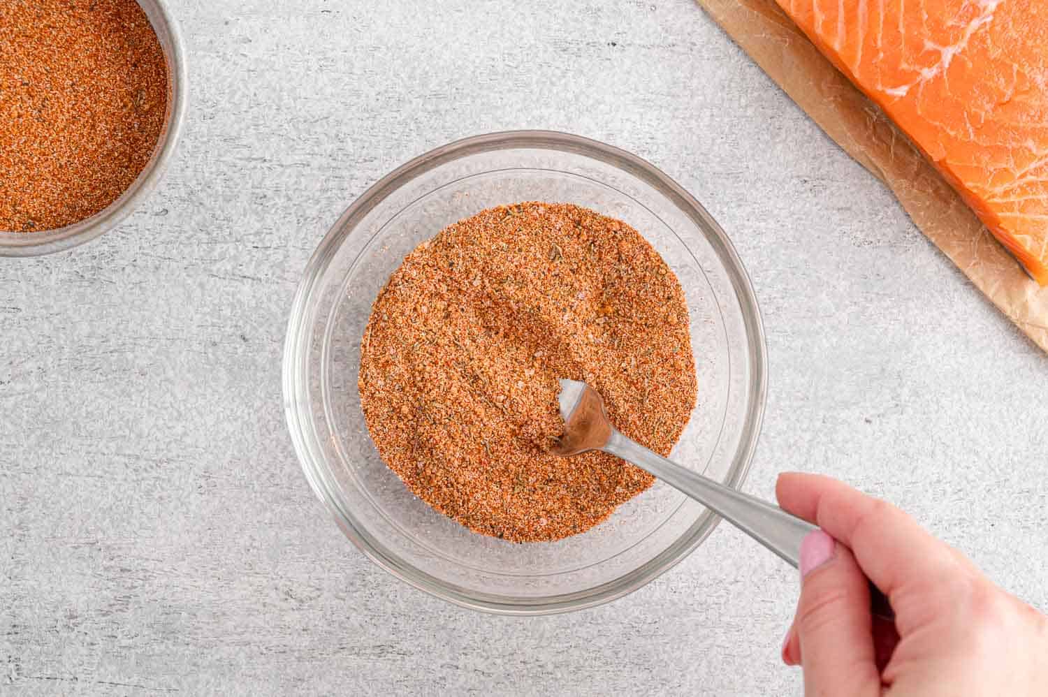 Spices in a small glass bowl, being mixed with a small spoon.