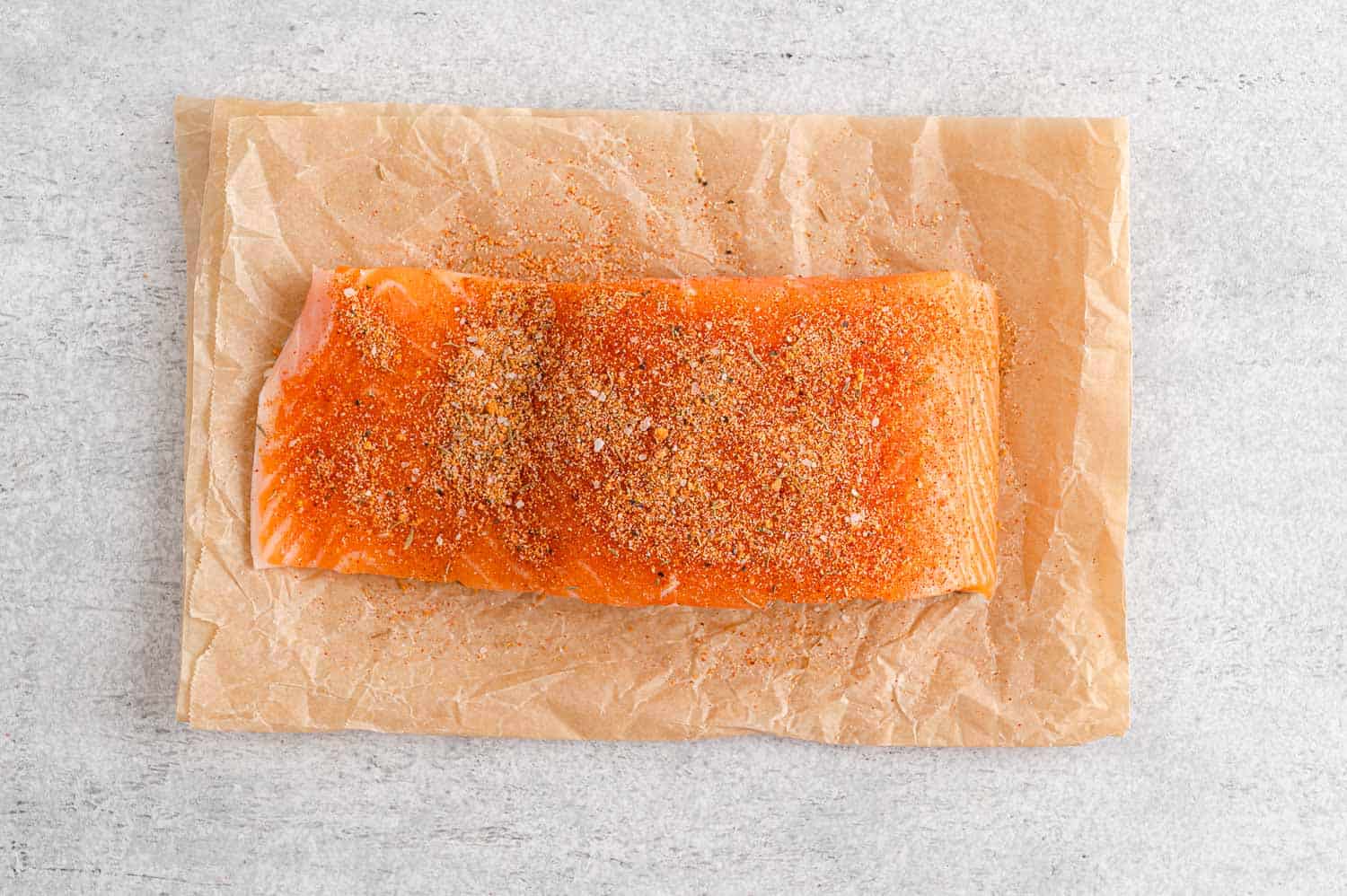 Piece of raw salmon on top of parchment paper, sprinkled with salmon seasoning.
