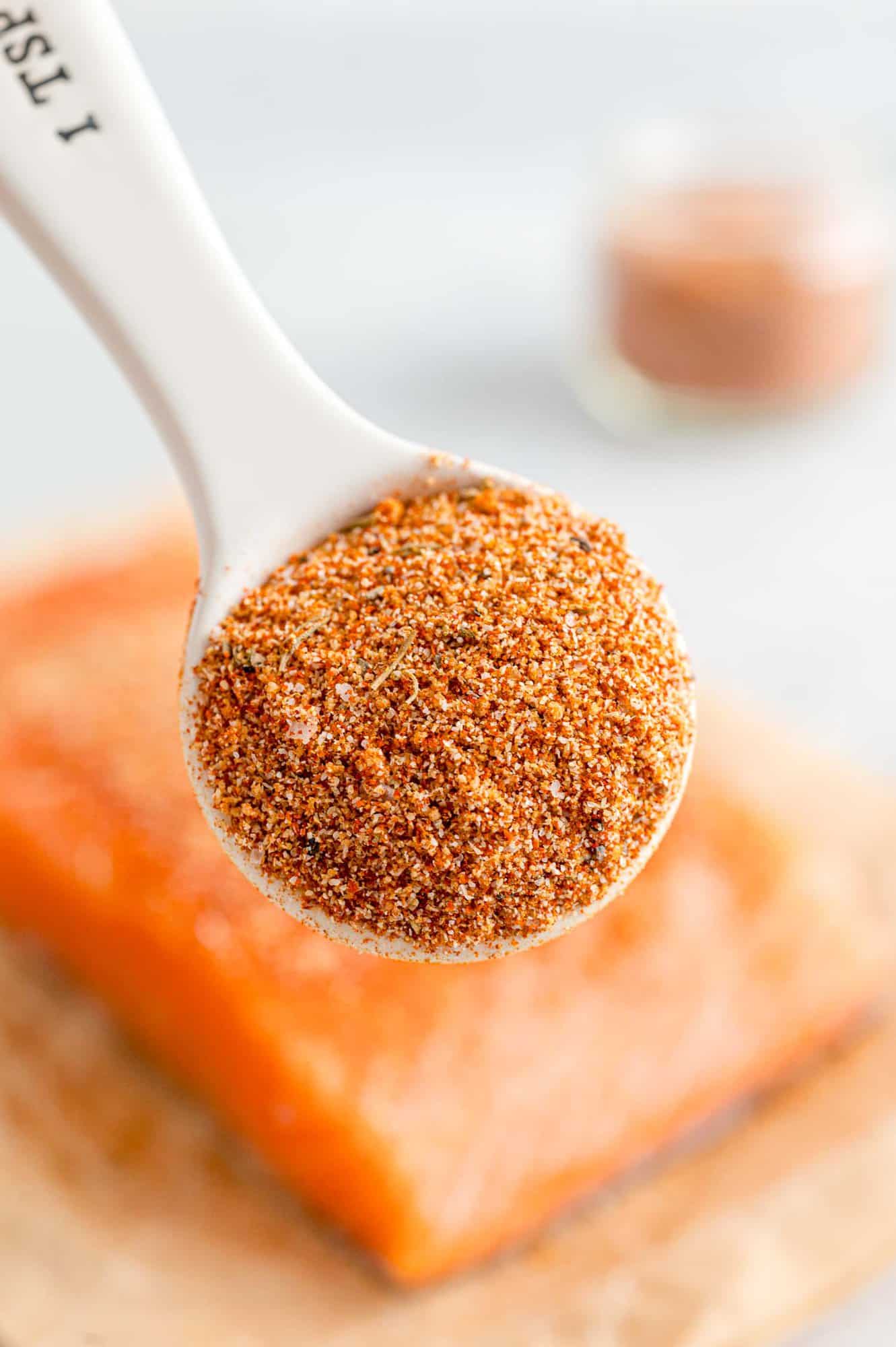 Spoonful of salmon seasoning being held in front of a fillet of raw salmon. 