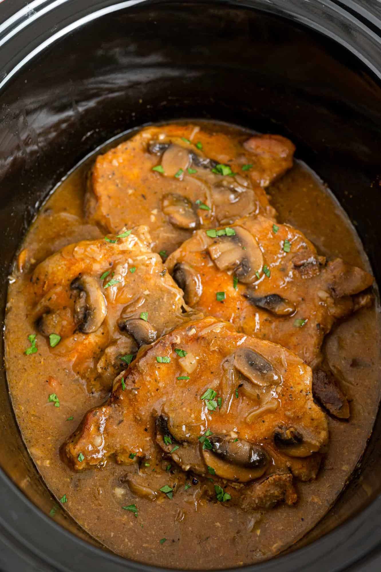 Overhead view of pork chops covered in mushroom and onion gravy inside the slow cooker.