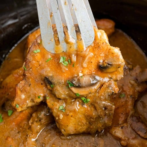 Slow cooker pork chop held with tongs.