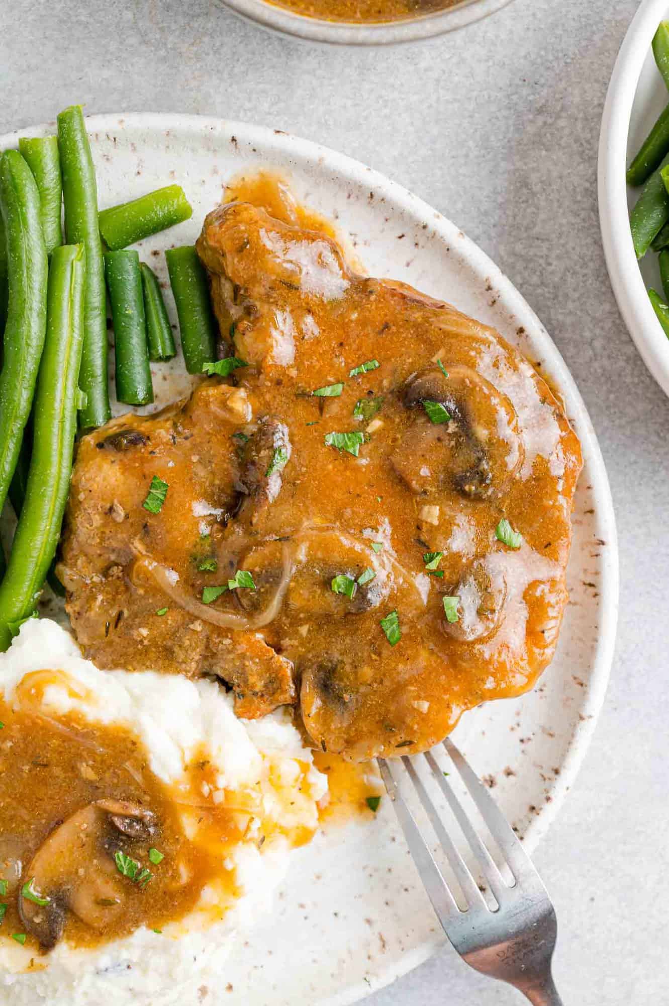 Overhead view of slow cooker pork chops served on a plate, covered in gravy next to mashed potatoes and green beans.