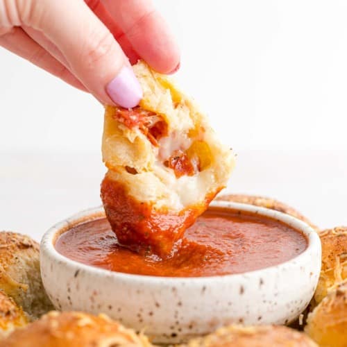 Stuffed pizza bite being dipped into marinara sauce.