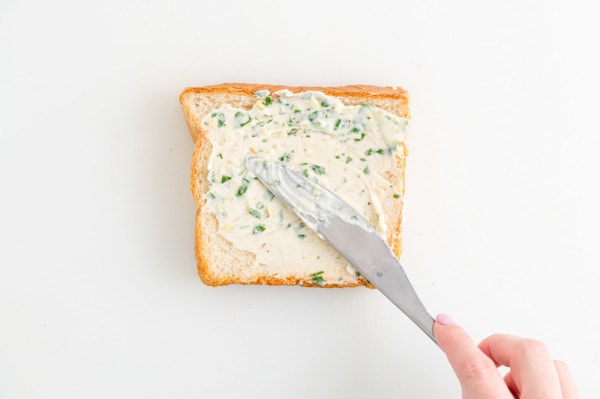 A hand using a knife to spread garlic butter over a slice of Texas toast.