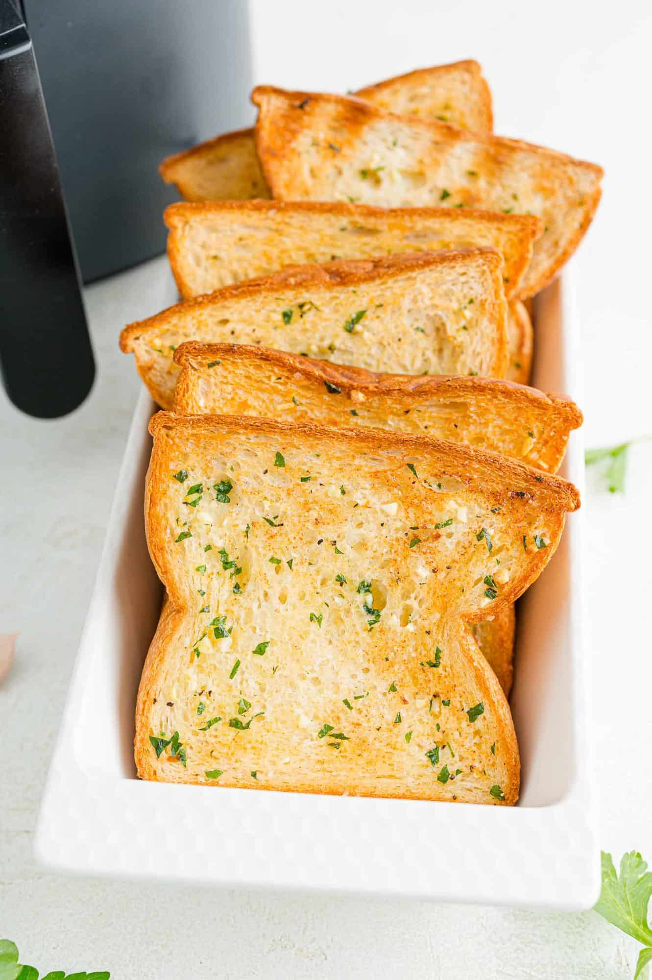 Slices of Texas toast garlic bread in a long rectangular serving tray, next to the air fryer.