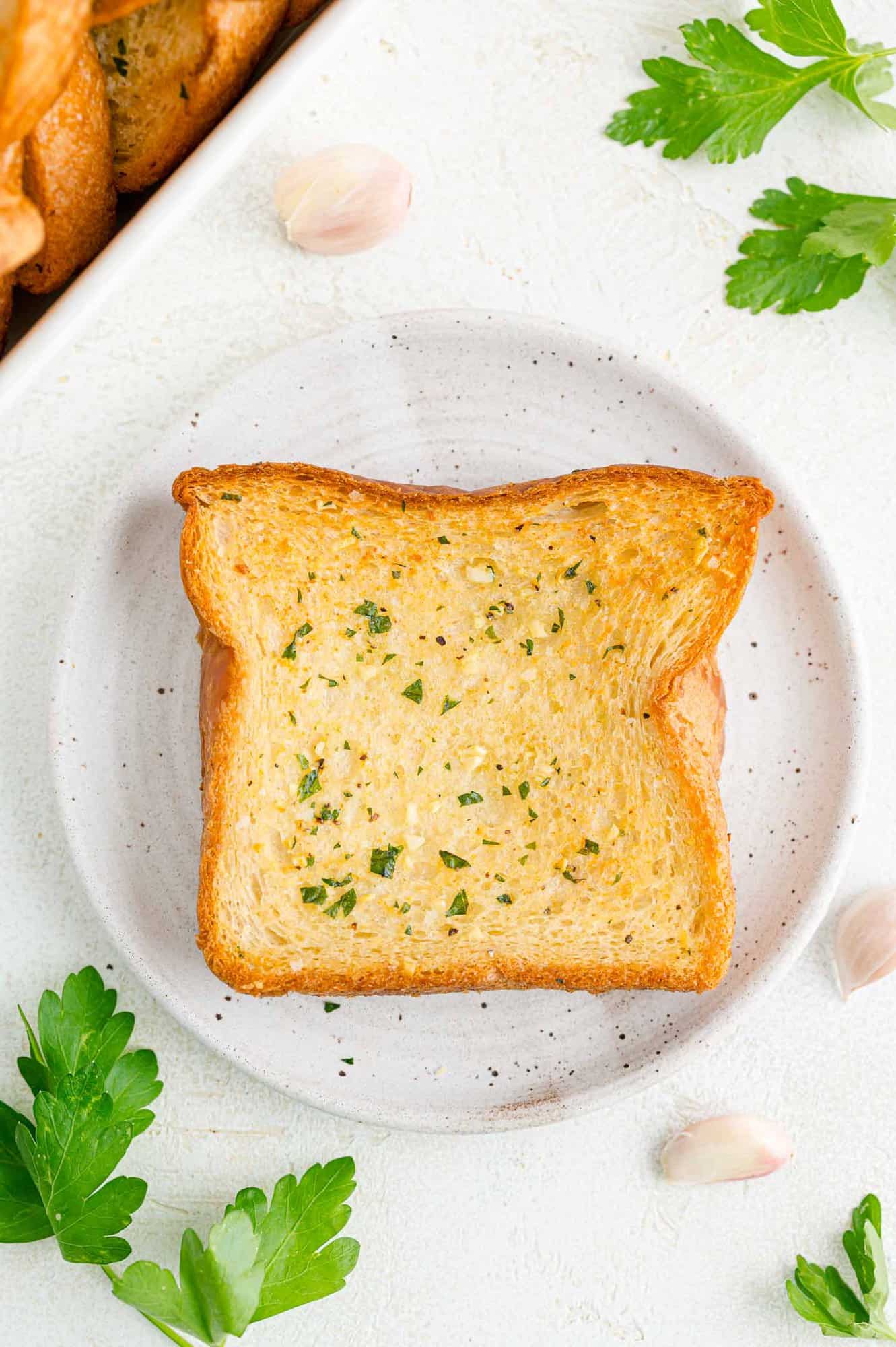 Turn fluffy Texas toast into the best homemade garlic bread with this easy recipe, with instructions for the oven, grill, and air fryer. Overhead view of slices of Texas toast garlic bread on a white plate.