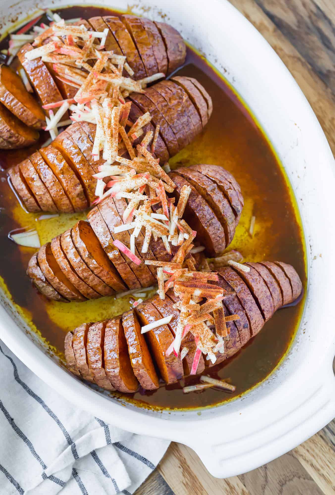 Hasselback sweet potatoes in a white baking dish with apples on top.