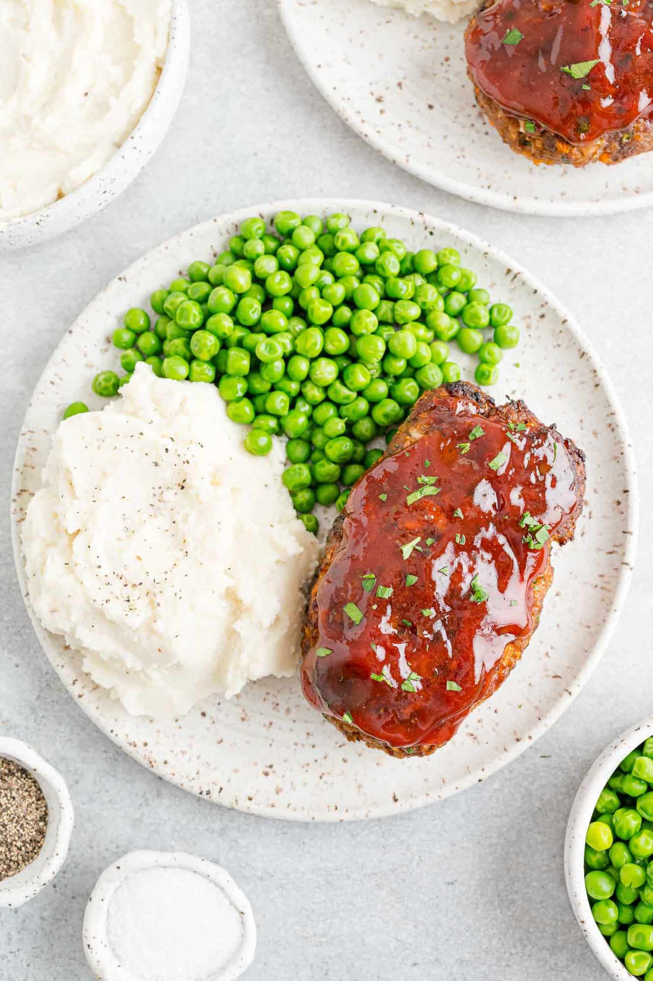 Air fryer meatloaf on a plate with peas and mashed potatoes.