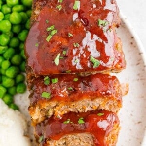 Air fryer meatloaf, cut into slices, on a place with peas and potatoes.