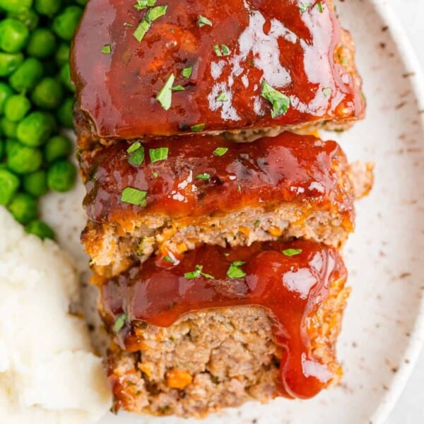 Air fryer meatloaf cut into slices, served with potatoes and peas.