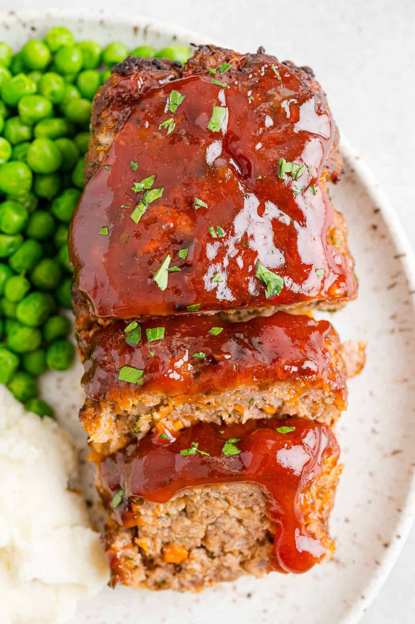 Air fryer meatloaf, cut into slices, on a place with peas and potatoes.