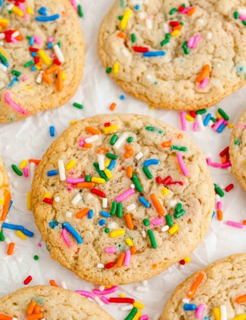 Funfetti cookies on a white surface, sprinkled with additional jimmies.