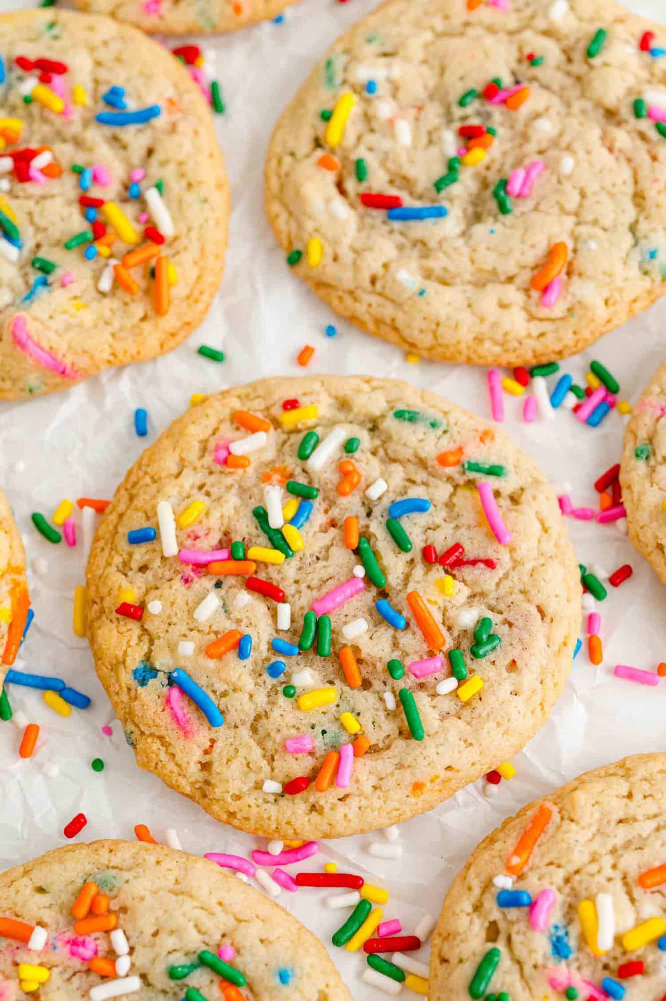 Funfetti cookies on a white surface, sprinkled with additional jimmies.