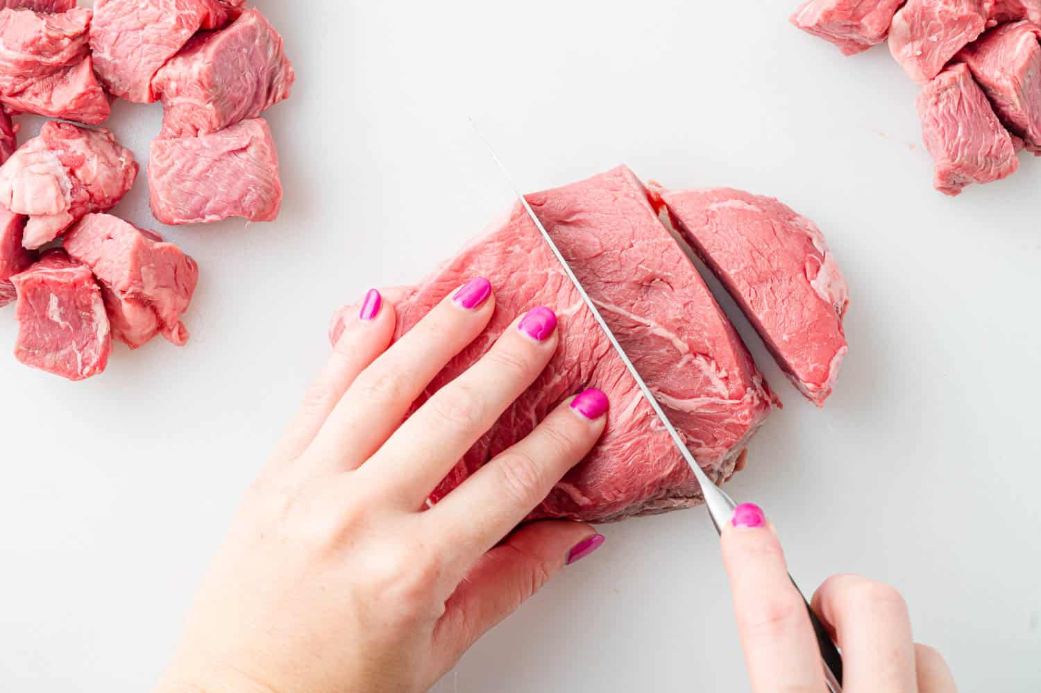 Raw steak being cut into bites.