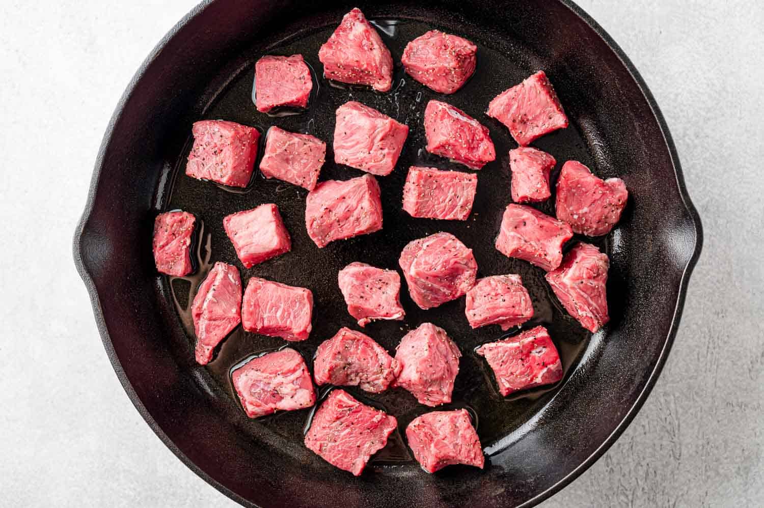 Uncooked steak bites in a single layer in pan.