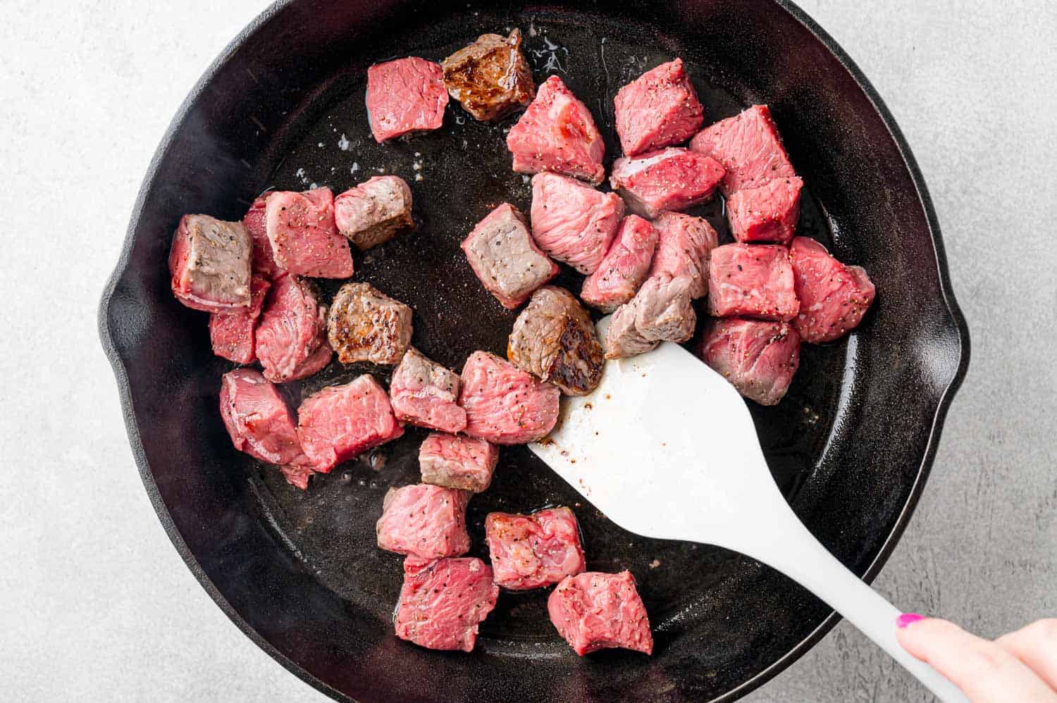 Half cooked steak bites, being stirred with a spatula.