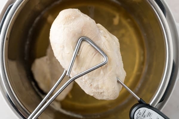 Cooked chicken held over iInstant Pot, being checked with a thermometer.