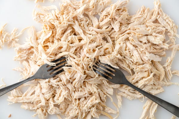 Chicken being shredded with two forks.