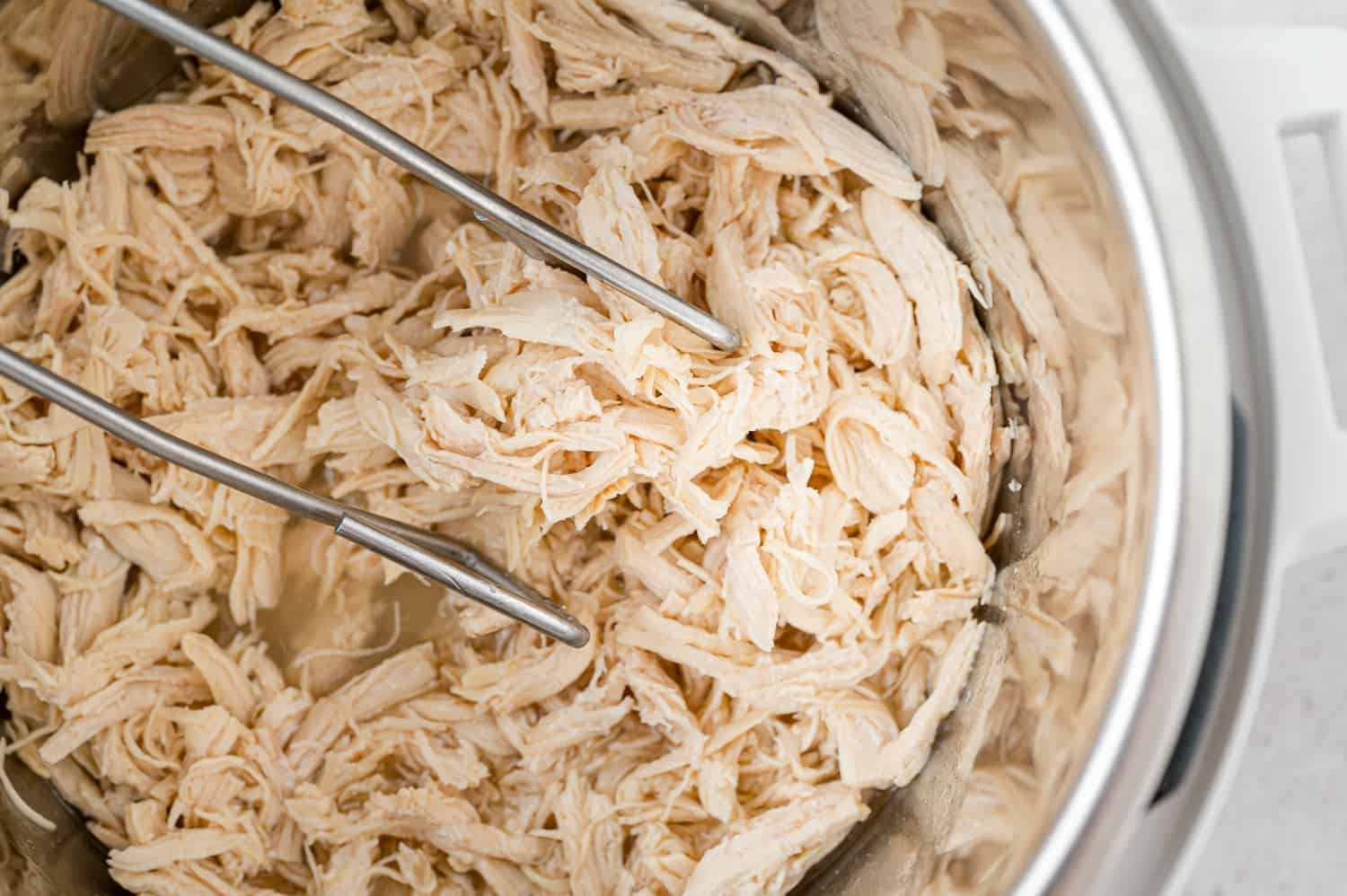 Shredded chicken in Instant Pot, held with tongs.