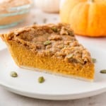 Slice of pumpkin pie with streusel on a white plate.