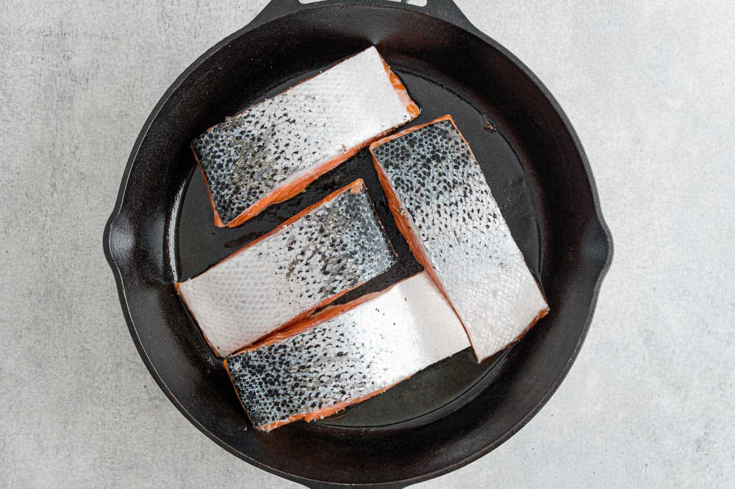 Salmon fillets in frying pan, skin side up.