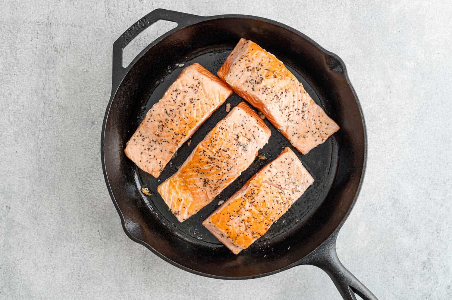 Salmon fillets face up in frying pan, lightly browned.
