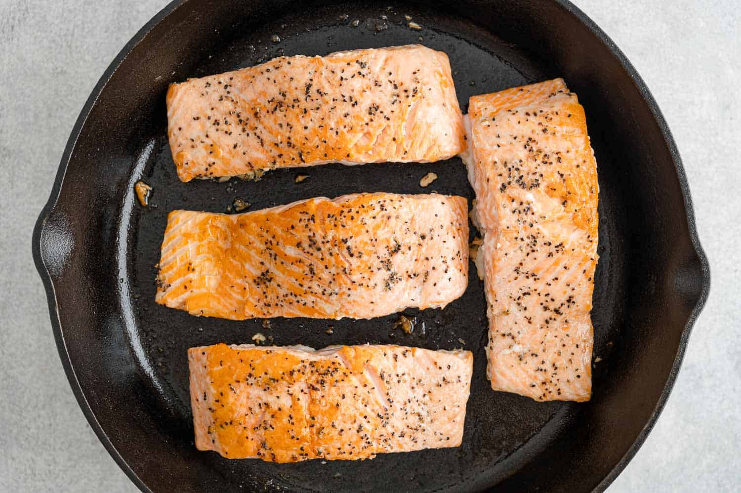 Cooked salmon fillets in a black skillet.