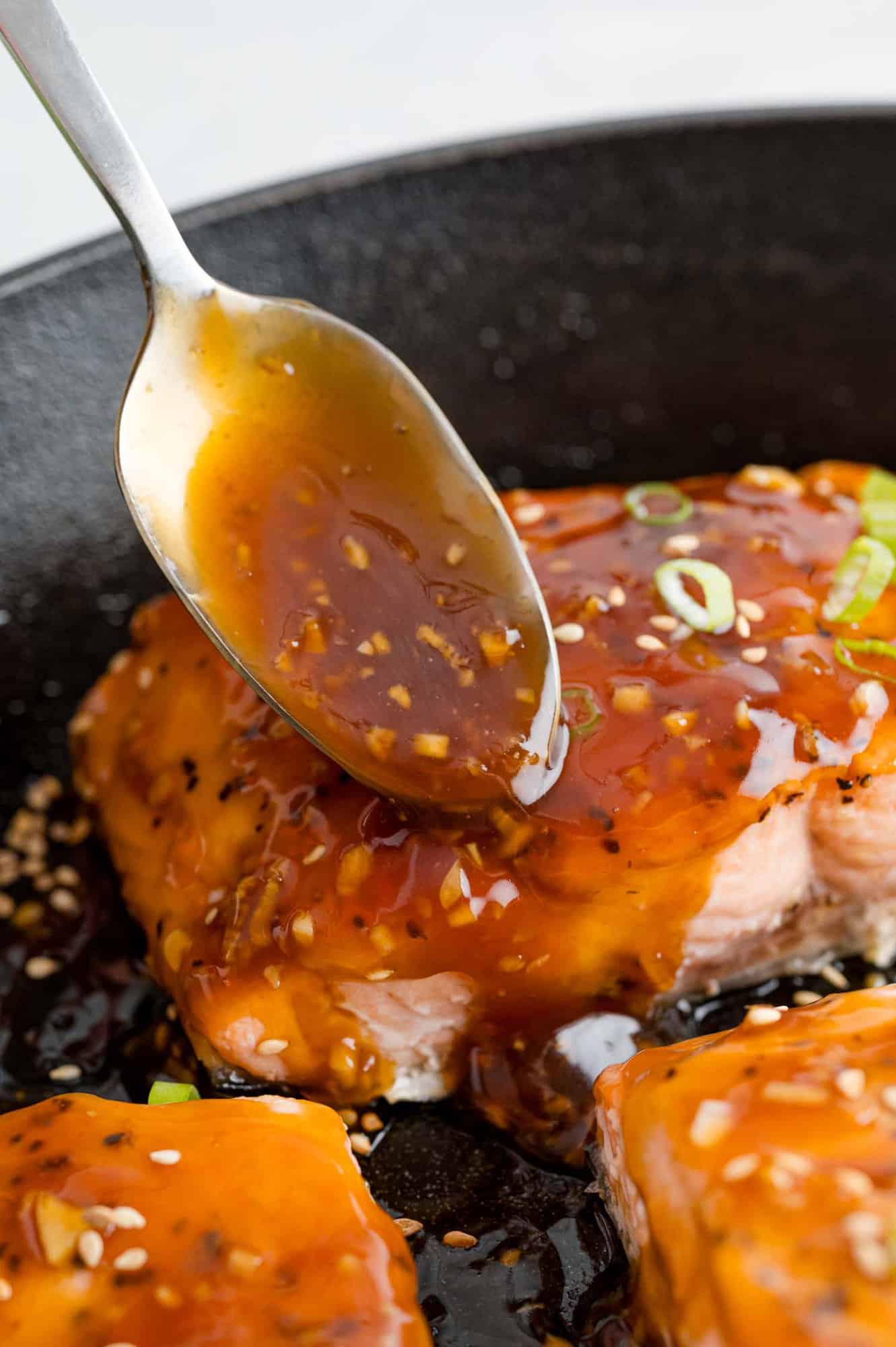 Teriyaki sauce being spooned onto salmon fillet.