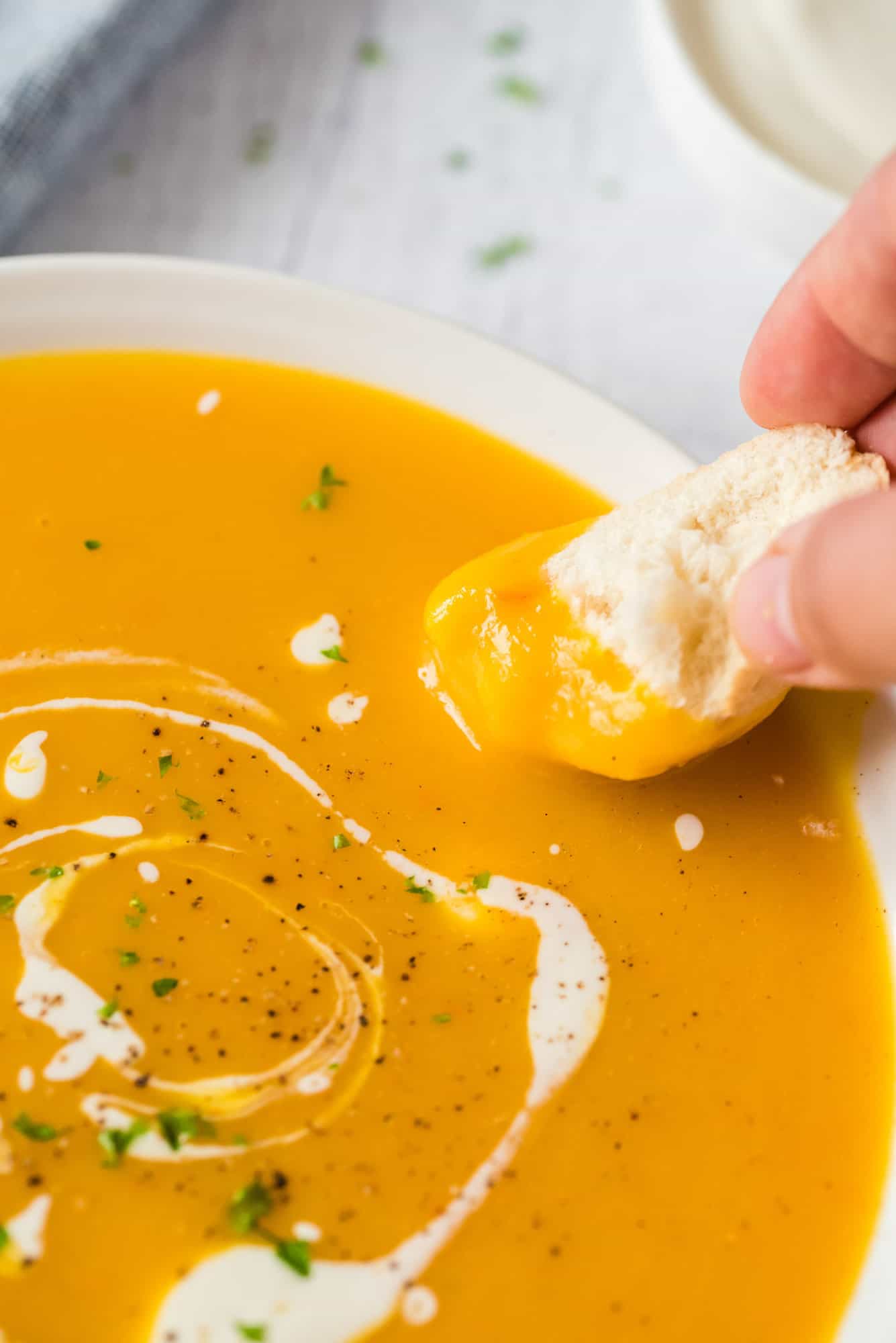 A hand dips a piece of bread into a bowl of pumpkin soup.