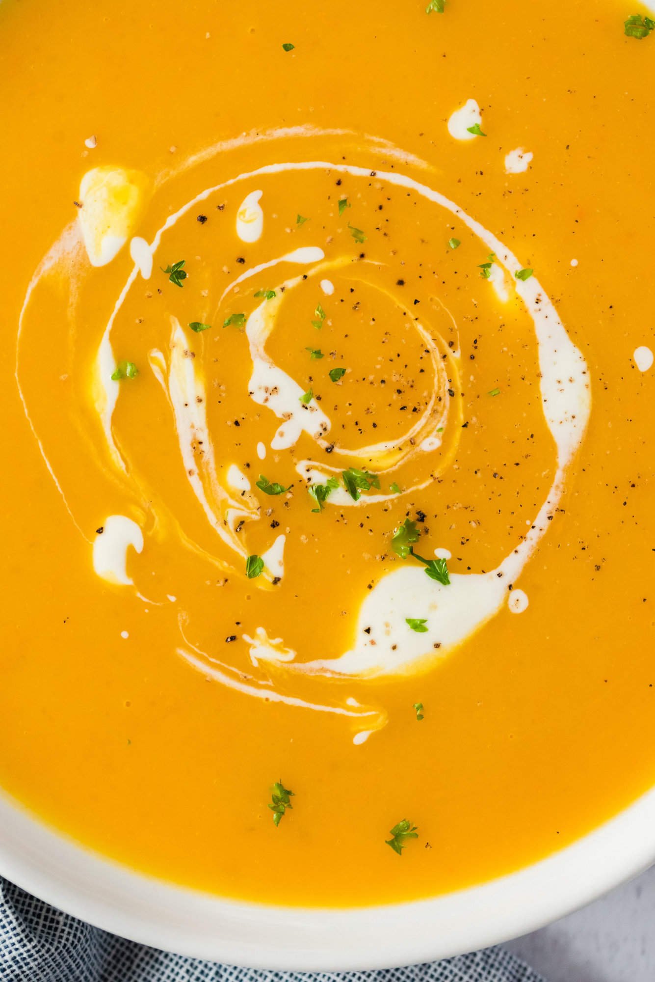 Close up overhead view of pumpkin soup in a bowl with a swirl of cream.