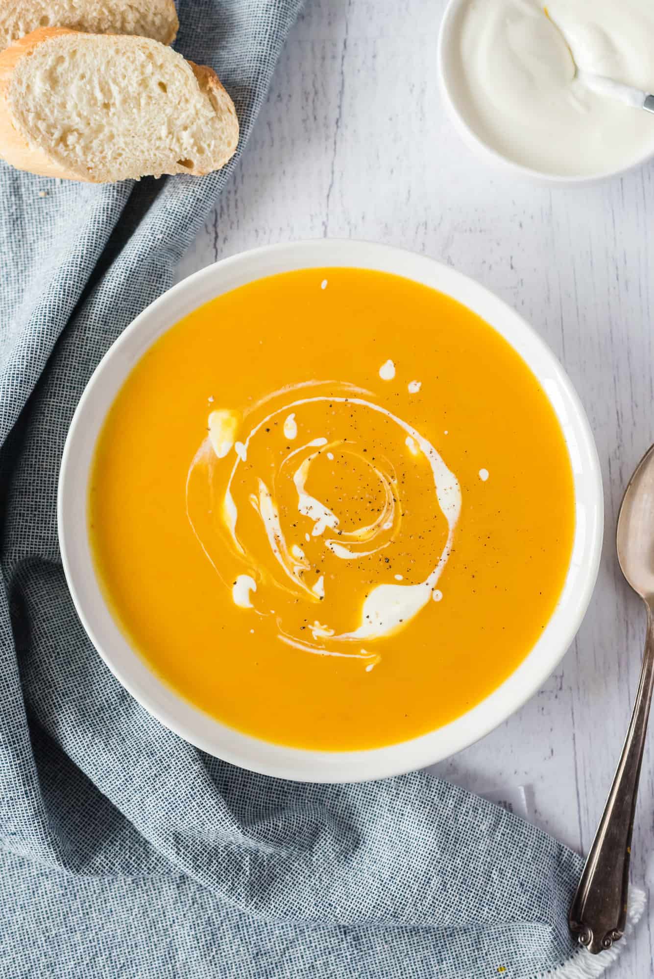 This creamy crockpot pumpkin soup recipe is velvety smooth, filled with hidden veggies, and perfect for fall. Made with only 5 ingredients! Overhead view of a bowl of slow cooker pumpkin soup swirled with cream.