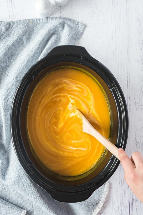 Cream being stirred into pumpkin soup inside the slow cooker.