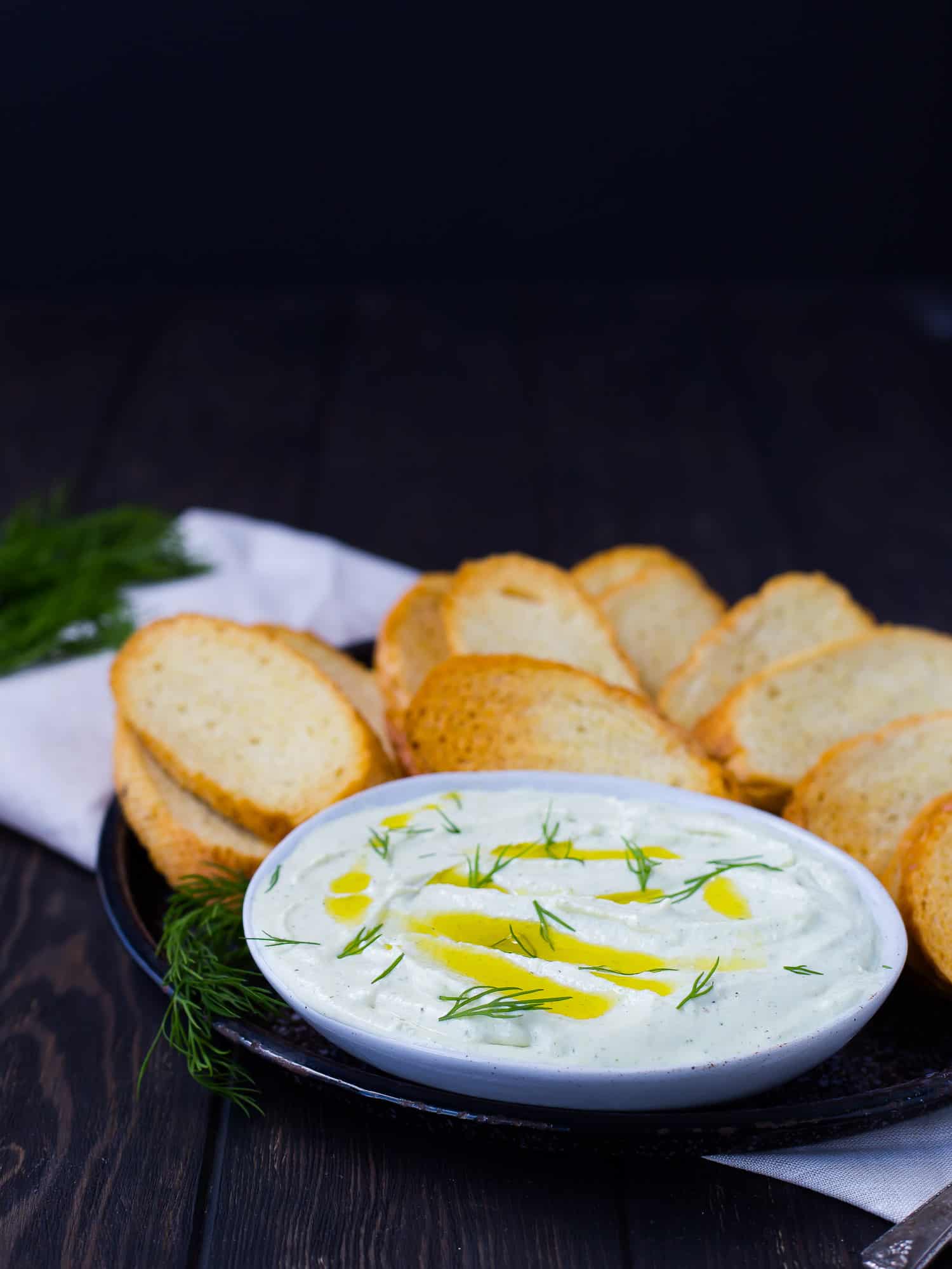 Whipped feta in a shallow bowl, surrounded by crostini, black background.