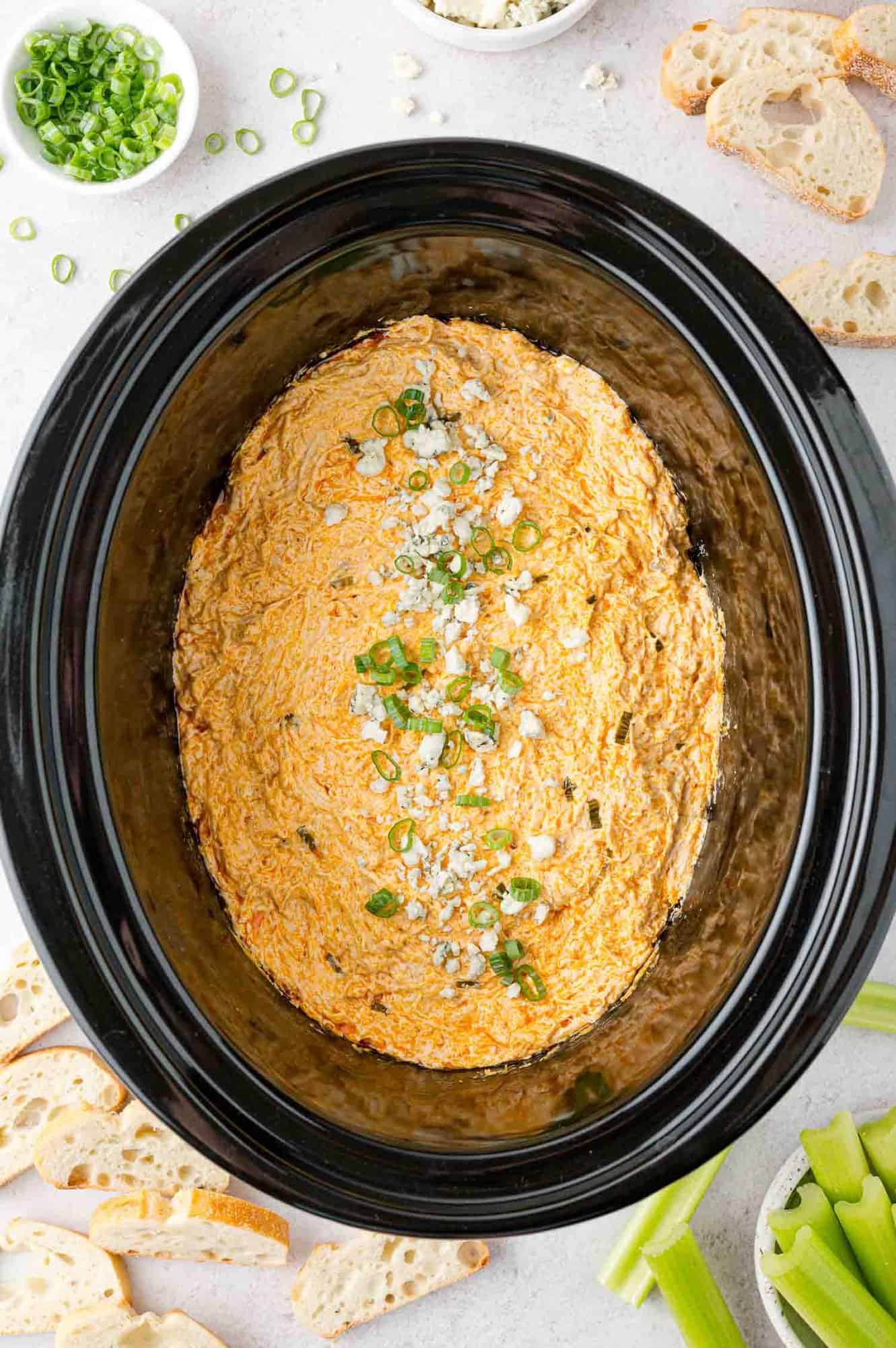 Crockpot buffalo chicken dip garnished with green onions and blue cheese.