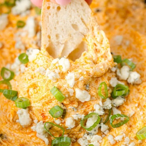Crockpot buffalo chicken dip with a piece of bread being dipped into it.