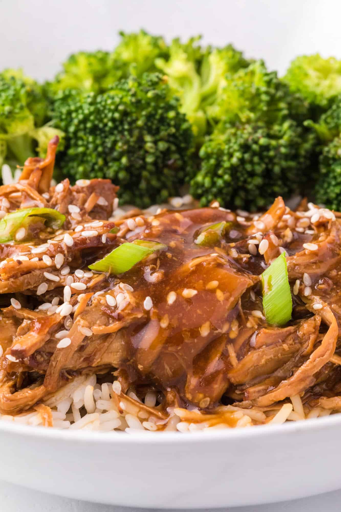 Close up of teriyaki chicken served next to broccoli in a bowl of white rice.