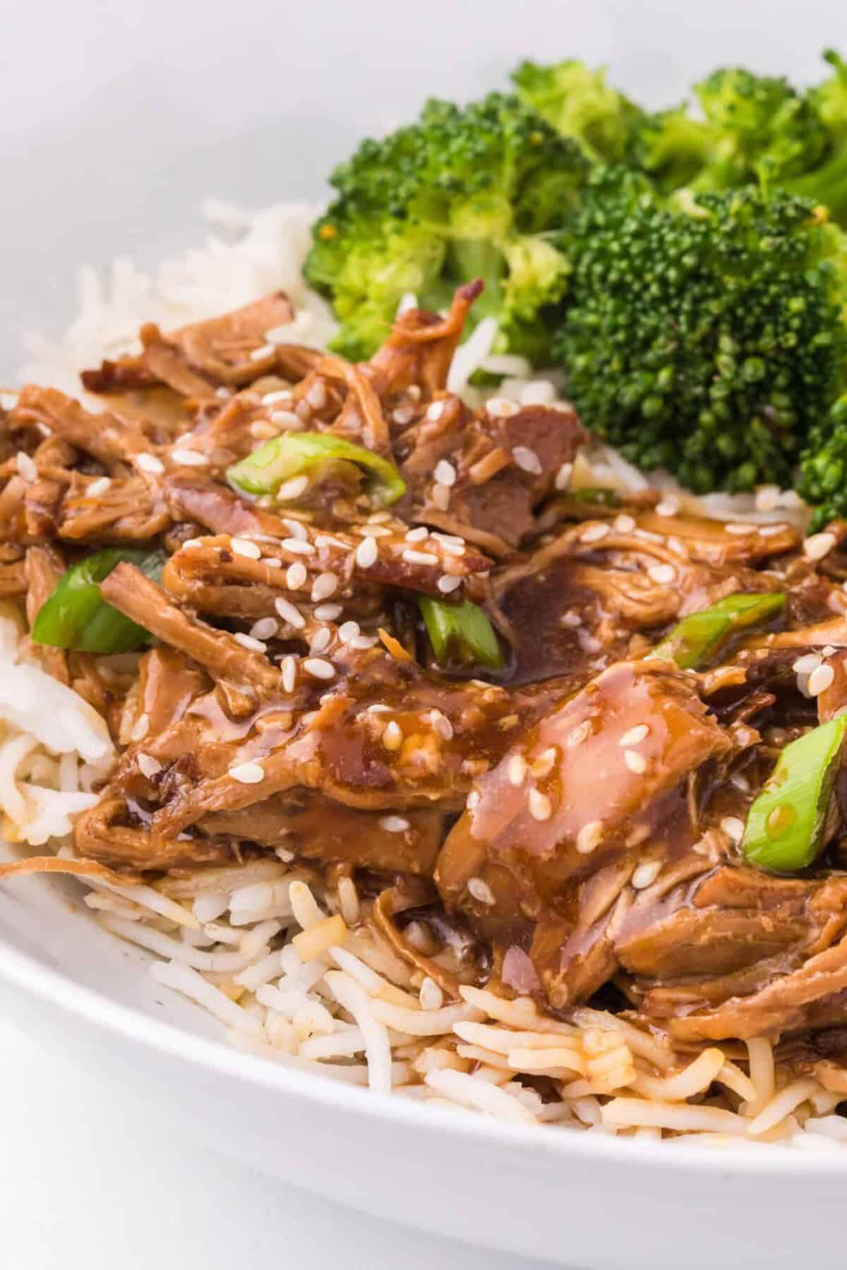 Close up of instant pot teriyaki chicken served next to broccoli in a bowl of white rice.