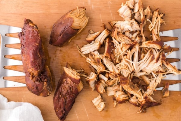 Partially shredded teriyaki chicken on a wooden cutting board next to meat shredding claws.