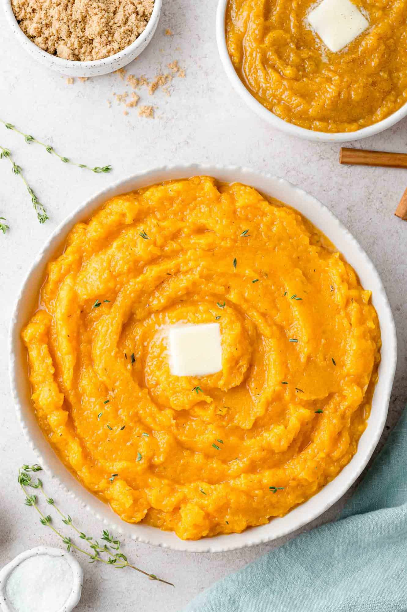 Savory mashed butternut squash in a large bowl, topped with butter. Sweet version also partially visible.