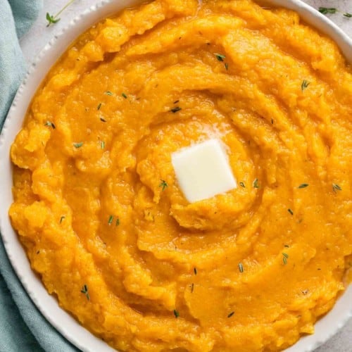 Mashed butternut squash in a large bowl, topped with butter and thyme.