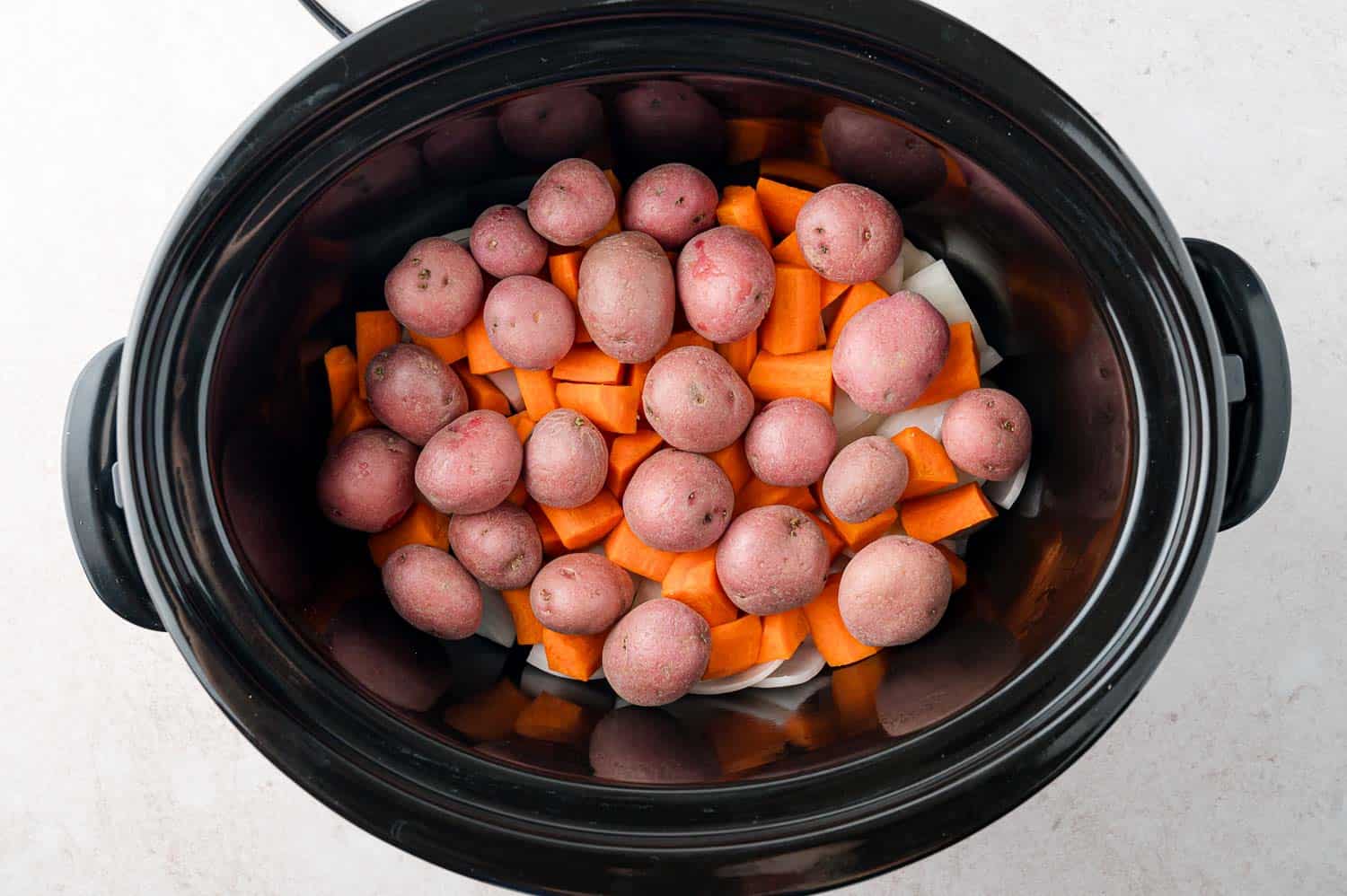 Uncooked potatoes and carrots in slow cooker.