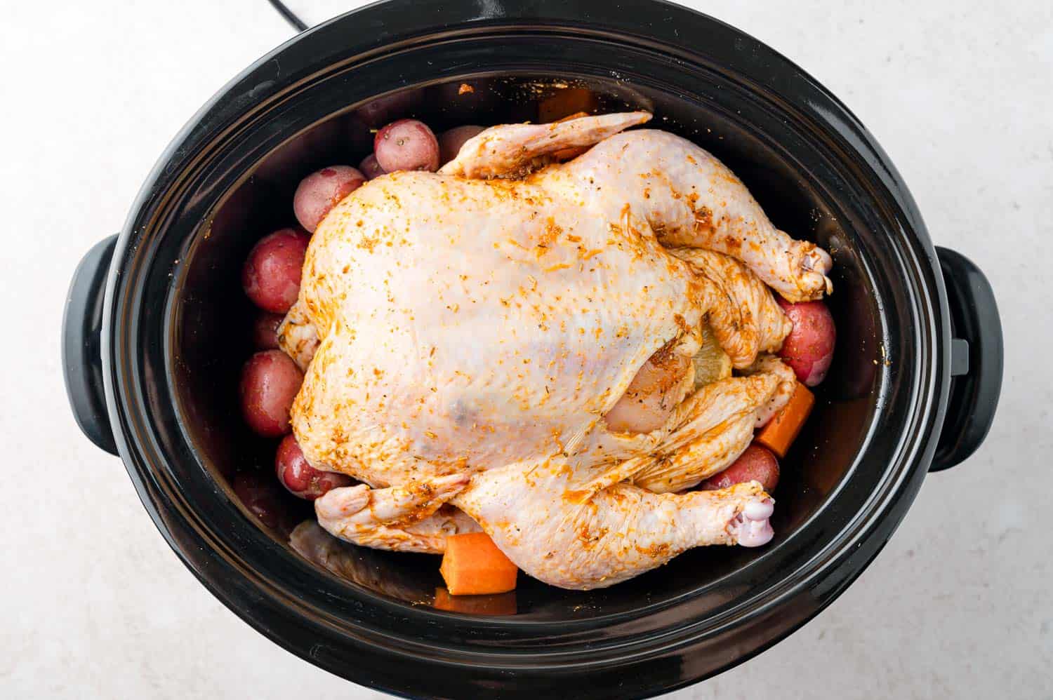 Uncooked chicken placed on top of potatoes and vegetables.