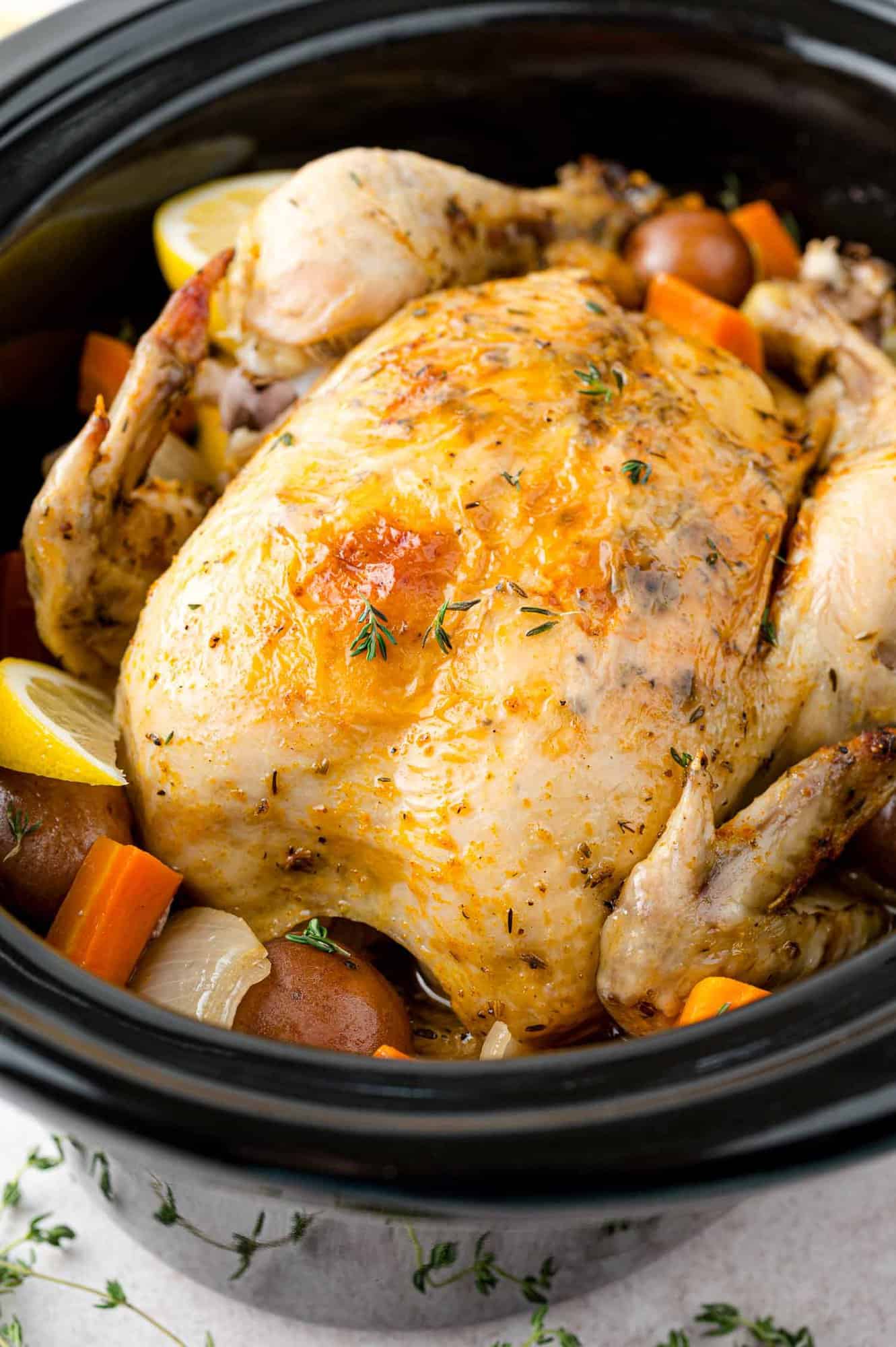 Whole chicken, pictured in a crockpot with carrots and potatoes.