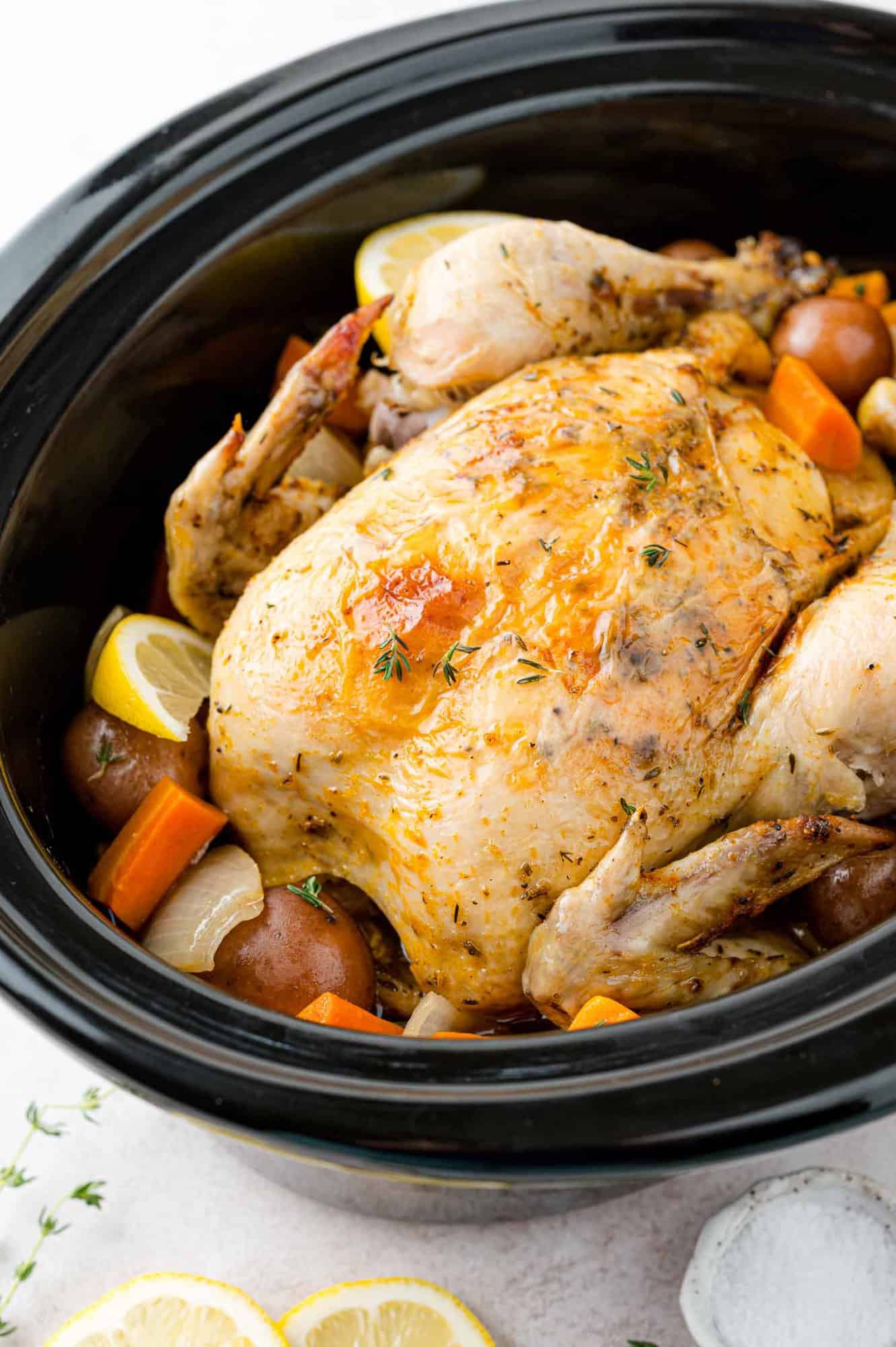 Whole chicken in a crockpot with vegetables and potatoes.