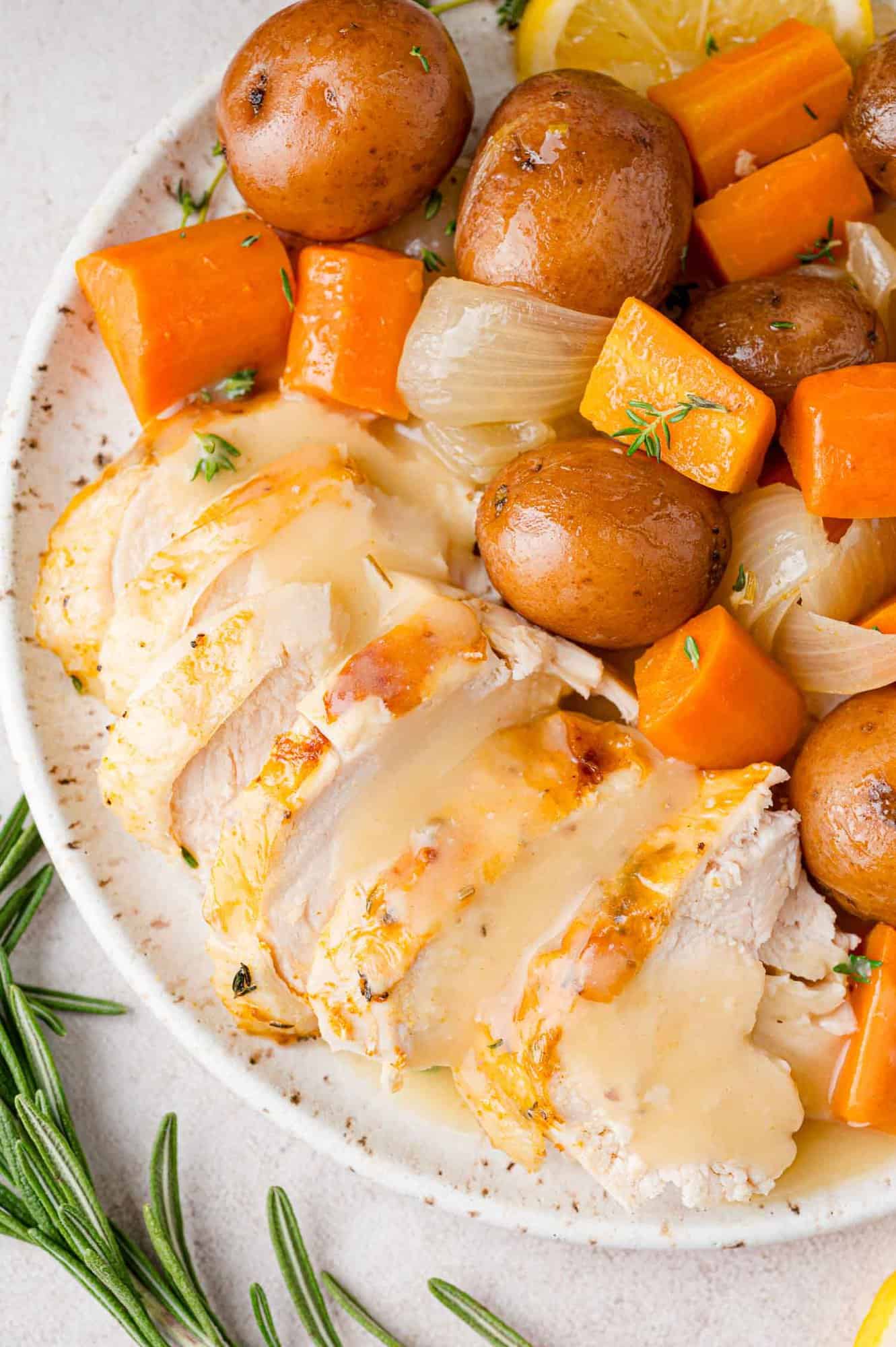 Sliced chicken and gravy on a platter with potatoes and carrots.