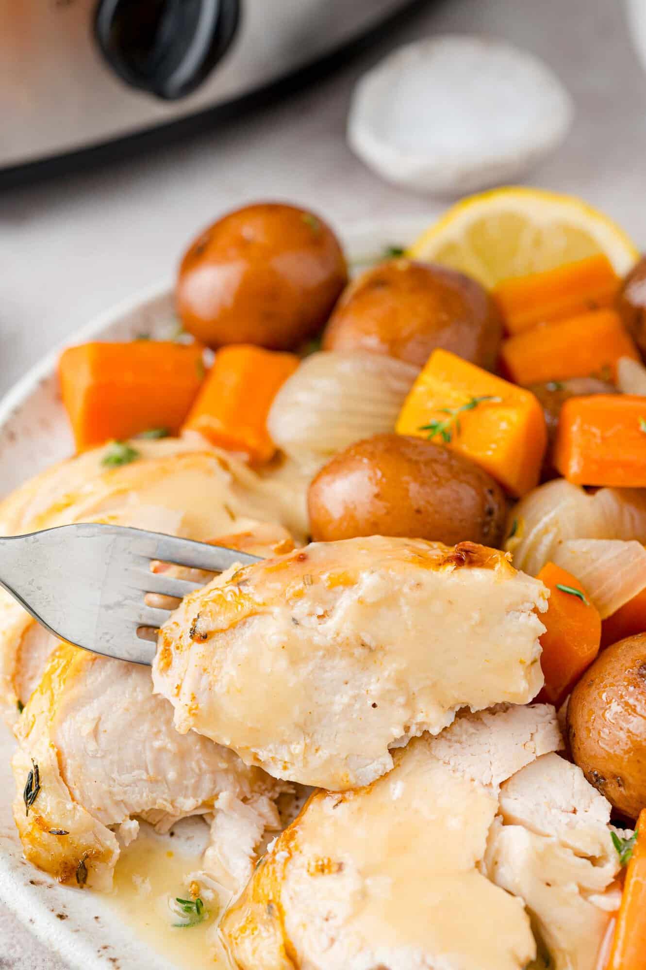 Piece of chicken on a fork, vegetables and potatoes in the background.