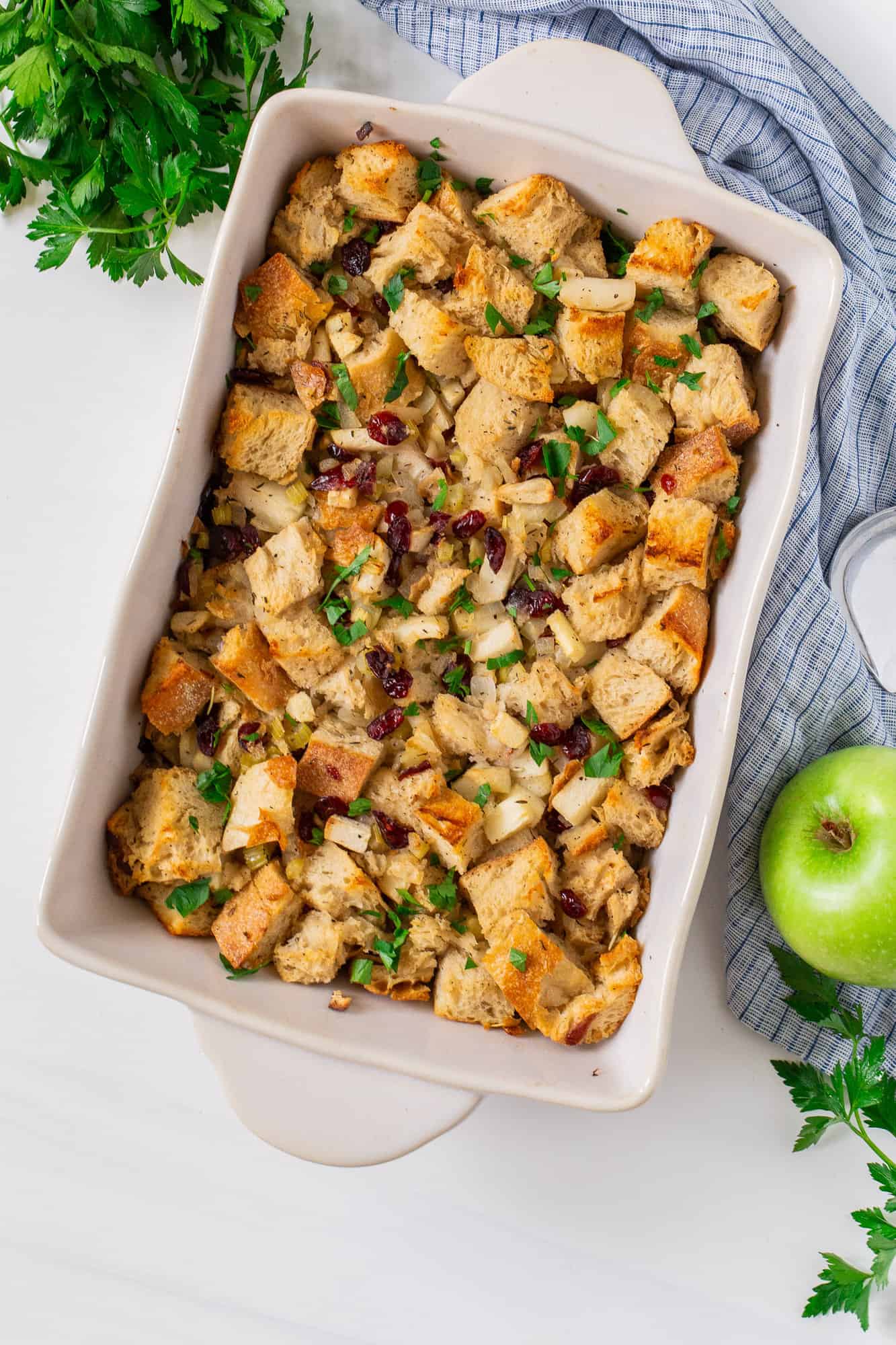 Apple stuffing in an off white casserole dish, with an apple nearby.
