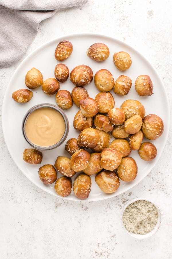 Overhead view of soft pretzel bites arranged around a bowl of cheese sauce on a white plate.