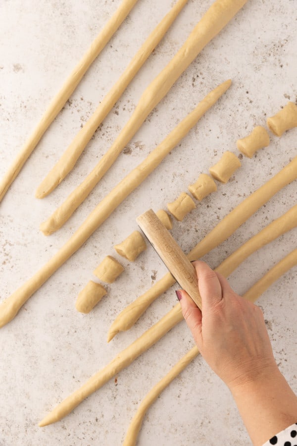 A hand using a dough cutter to cut ropes of pretzel dough into small bite-sized pieces.